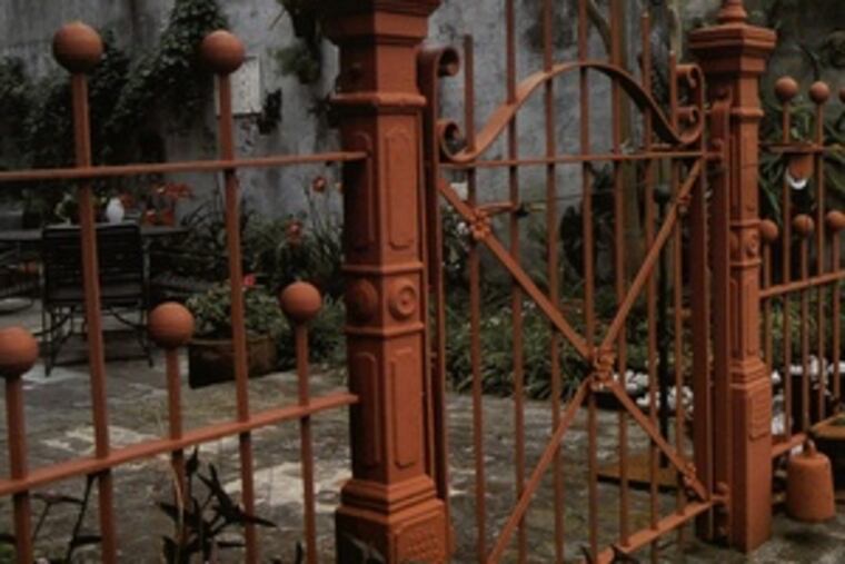 The enclosed pool area, called a piscine, of this hidden garden is separated by an antique cast-iron fence, painted a delicious rusty pink. The house behind the pool is elegant, its architecture more influenced by Spanish colonizers than by French.