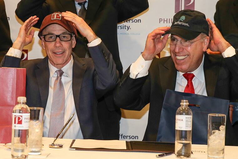 Thomas Jefferson University and Philadelphia University announced a preliminary agreement to merge. At the signing table (from left): Staphen Klasko MD MBA President and CEO, Jefferson, and Stephen Spinelli, Jr., PhD, President, Philadelphia University, trade ball caps after signing the agreement.