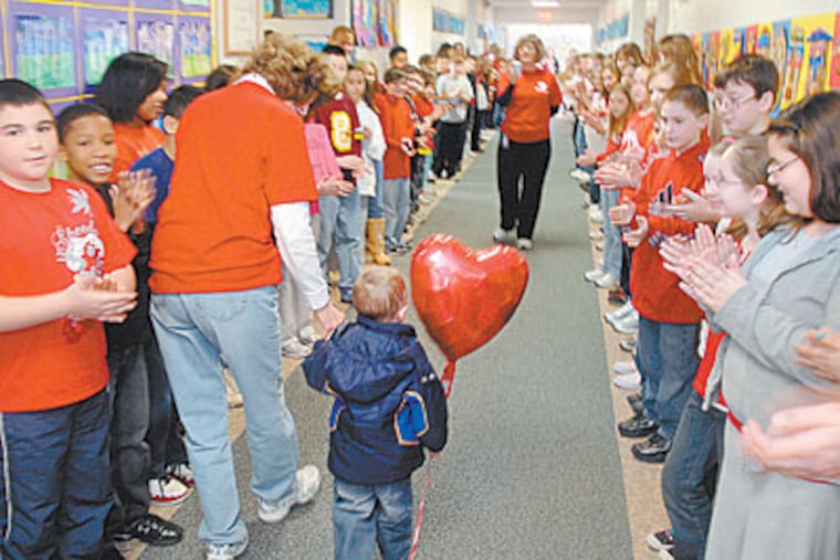 It was all about the heart yesterday as 3-year-old transplant recipient Christopher Ennis was greeted by schoolchildren in Marlton. Leading him down the hall is teacher Mary Ellen Walls. (TOM GRALISH / Staff Photographer)