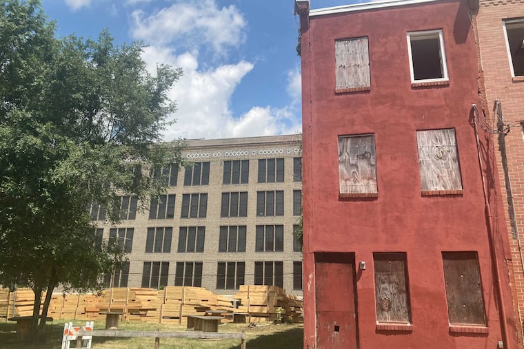 A PHA-owned vacant home and a lot serving as a staging ground for construction in Sharswood, with the former Reynolds public school in the background.