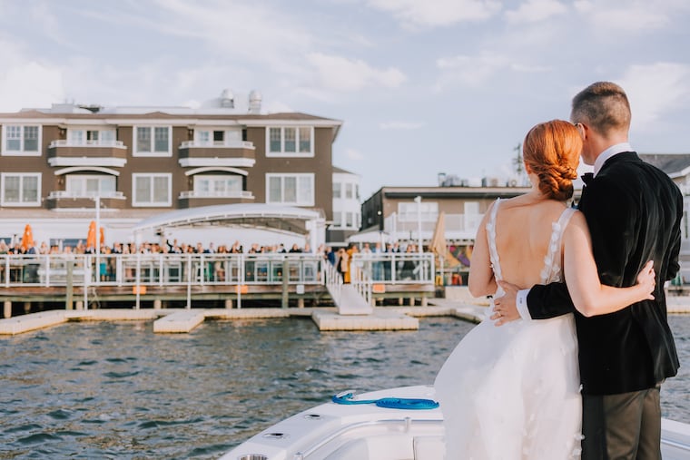 A newly married couple looks out at their wedding guests, who are celebrating on the deck of The Reeds at Shelter Haven in Stone Harbor.