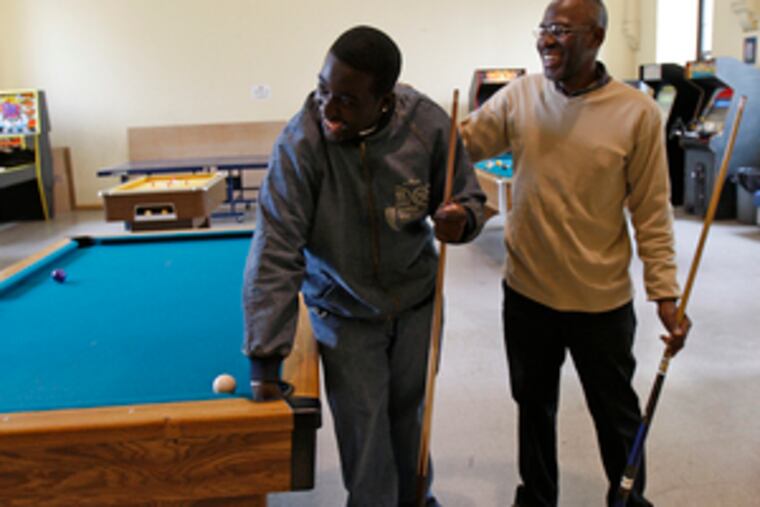 Community outreach worker Carl Burman (right) laughs with Jay-R Mills, of Southwest Philly, after a game of pool inside Myers Recreation Center.