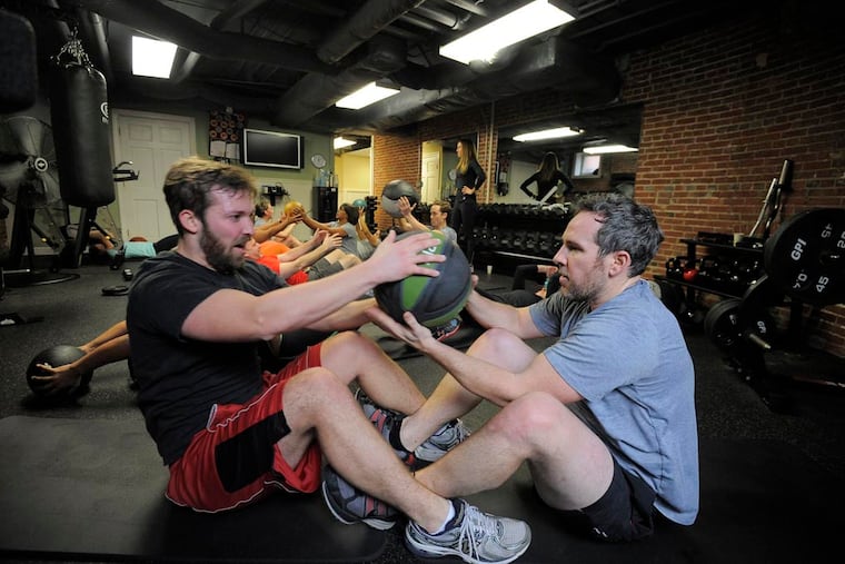 Left to right, Woody Heffern, marketing, and Jared Kelly, director of marketing, Agora Inc. pass a medicine ball while doing sit ups. Committing to new year's resolutions like going to the gym means keeping expectations realistic so as not to lead to disappointment.
