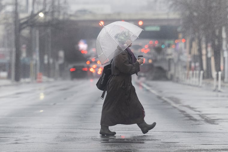 A woman shields herself from the rain with an umbrella as she crosses the street at 8th and Spring Garden Streets in Philadelphia on Thursday, March 5, 2026.