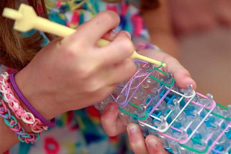 Weaving rubber bands on the Rainbow Loom, and finished bracelets on the crafter's wrist. (Akira Suwa/Staff Photographer)