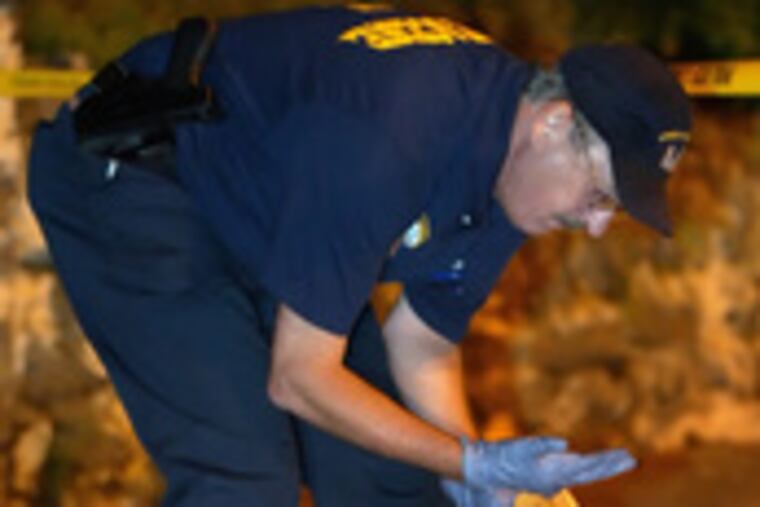 A police officer examines ballistic evidence yesterday while investigating a homicide at Broad Street and Lindley Avenue.