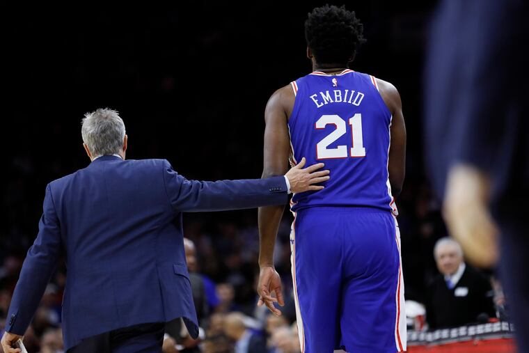 Sixers coach Brett Brown (left) walks Joel Embiid off the court after Embiid injured his finger against the Oklahoma City Thunder on Monday night.