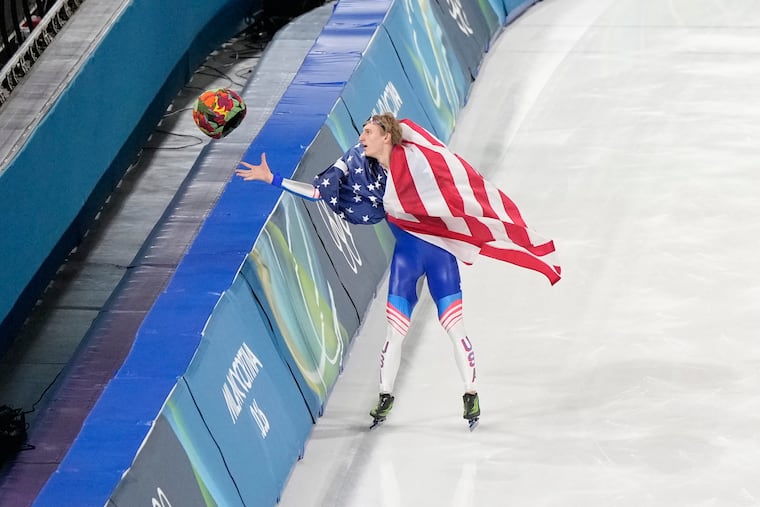 Jordan Stolz reaches for a helmet tossed from the crowd as he celebrates after winning the gold medal, setting an Olympic record, in the men's 500-meter speed skating final on Feb. 14.