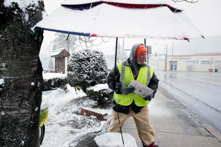 Newspaper vendor Roger Tize stands under his snow-covered umbrella on 1st Street in Coatesville, Chester County, as he sells papers Friday, March 20, 2015. ( ED HILLE / Staff Photographer )