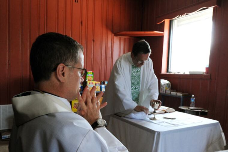 The Rev. William Murphy prepares the Eucharist as the Rev. Joseph Devlin contemplates. (CLEM MURRAY/Staff Photographer)