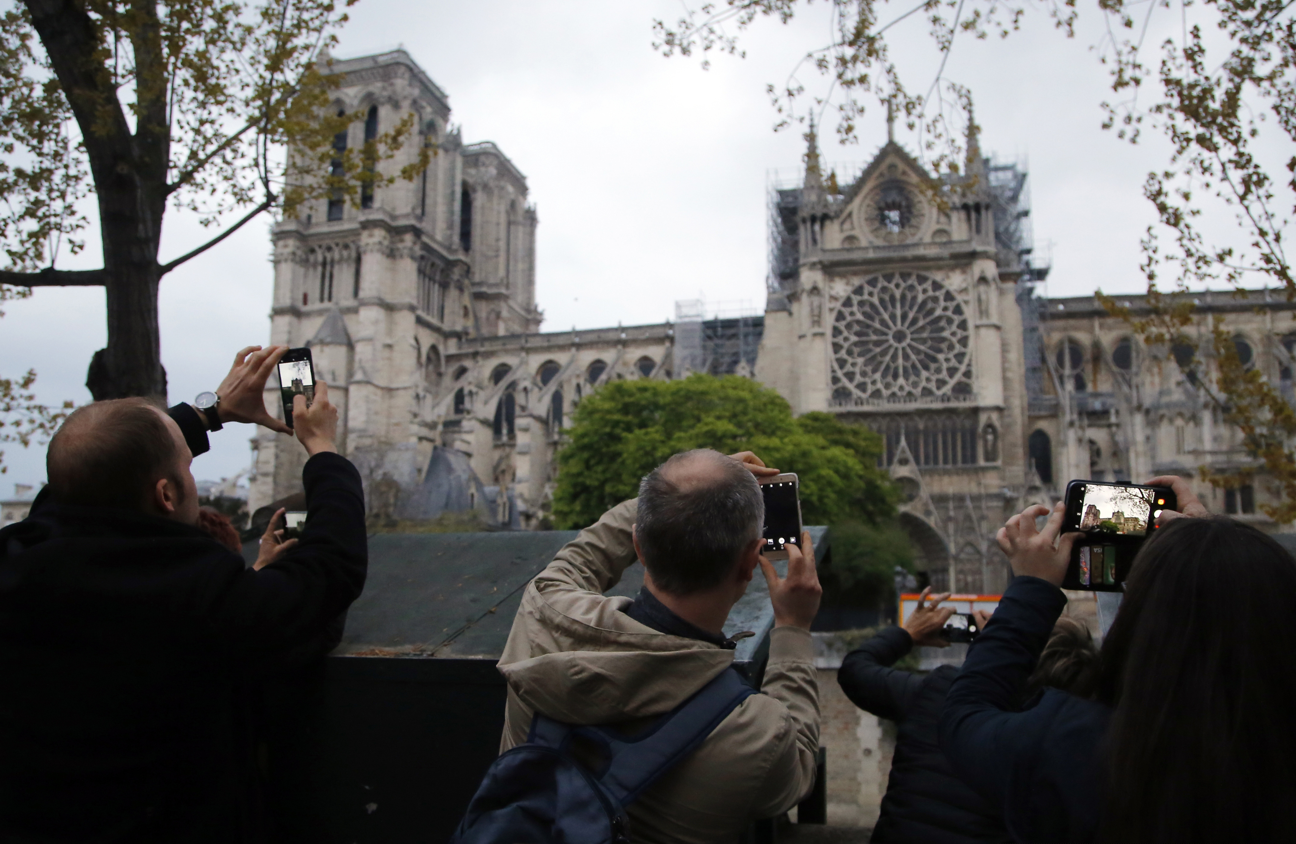 In this file photo dated Tuesday April 16, 2019, people take photos of the Notre Dame Cathedral in Paris, one day after a major blaze broke out at Paris' iconic cathedral.