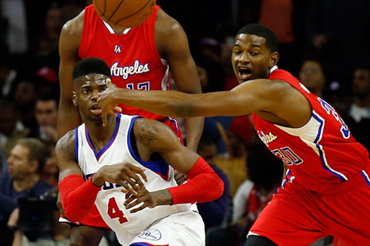 Sixers' Nerlens Noel passes the basketball from his knees past Clippers' C.J. Wilcox. (YONG KIM/Staff Photographer)