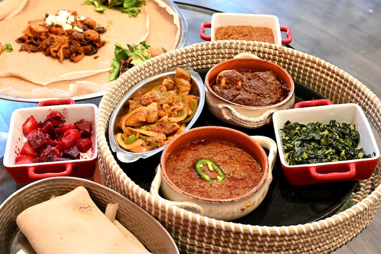 The injera combination platter at Buna Cafe in West Philadelphia July 28, 2021. Sides inside the round basket, clockwise from upper left are: Asa goulash; Doro wot; Gomen; and bozena shiro. Outside the basket, clockwise from lower left are injera bread (a spongy sour fermented flatbread); red beets and potatoes; quanta firfir and salad, resting on large Injera bread. and in rear, misir.