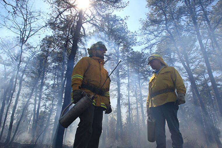 Doug Cutts, left, and Roger Montgomery, right, stand in a smoke-filled section of Wharton State Forest with the ignition devices during a March 24 prescribed burn. Firefighters battled another fire on Sunday and Monday in which 1,500 acres were burned. Investigators had not determined the cause of the fire. (CHARLES FOX / Staff Photographer/File)