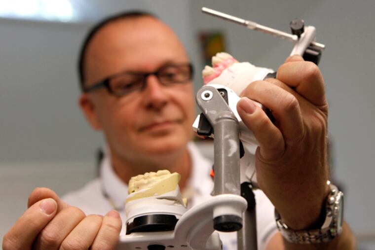 Hubert Jasinski, founder of Newtech Dental Laboratories, holds up a model jaw with dentures in it. The Newtech Dental lab is looking to expand, and will be breaking ground on an addition later this month. (LUKE RAFFERTY/Staff Photographer)