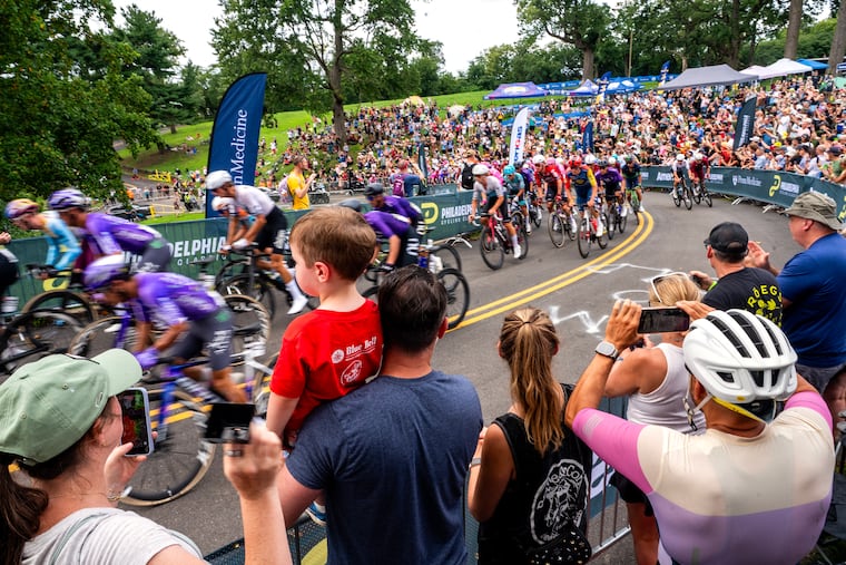 Heather Sobotkin (left) rings a cowbell while her husband, Lee Sobotkin, holds their son Elijah. 2, as the peloton makes its way through Lemon Hill in the men’s race during the Philly Cycling Classic in Philadelphia on Sunday. The family from Malvern were among the fans who cheered on the cyclists at the revived race.