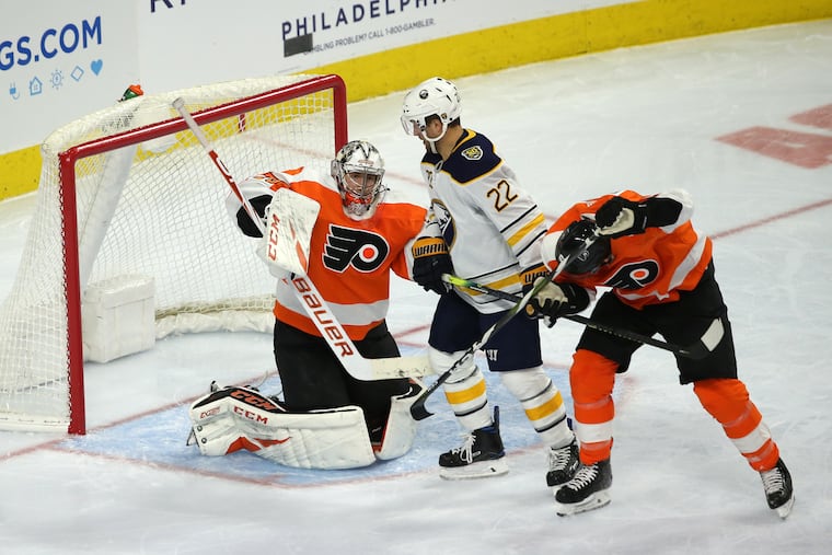 Carter Hart defends as Flyers defenseman Justin Braun (right) takes a puck to the helmet against Buffalo during Saturday night's second period. Buffalo's Johan Larsson is in the middle. The Flyers outlasted the Sabres, 3-1, at the Wells Fargo Center.