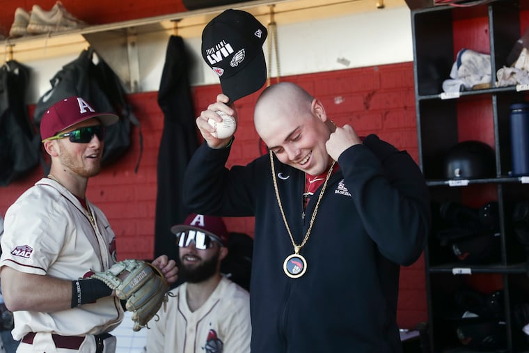 Luke Smith smiles while putting on a chain he received from Alex Madera, left, in the Arcadia dugout before their season-opener against Ursinus at Skip Wilson Field in Ambler, Pa., in February.