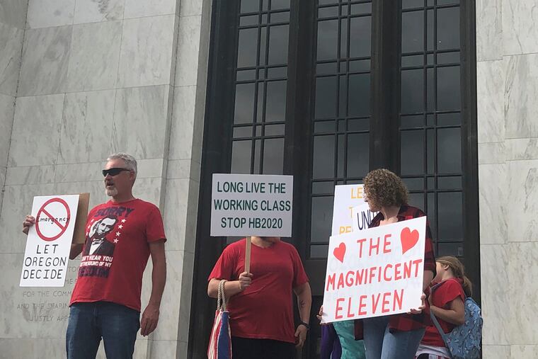 In this photo taken Sunday, June 23, 2019, local Republicans show their support for a Republican walkout outside the Oregon State Capitol in Salem, Ore. The gathering took place only a day after the Senate president ordered the statehouse to close over a "possible militia threat," the latest escalation in a Republican walkout over proposed climate policy that has put Democrats' top legislative priorities at risk.
