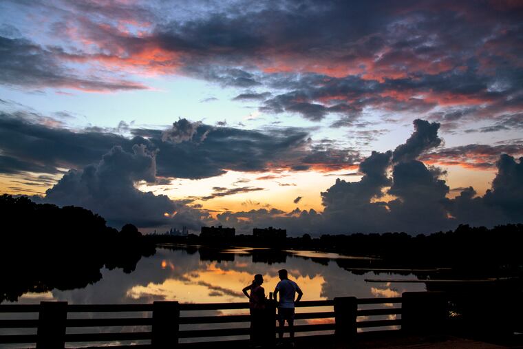 Diego and Lisa Improta of Collingswood watch the sunset over the still water of the Cooper River on Thursday after a day of scattered downpours and flood watches. They were standing on the Cuthbert Blvd bridge right on the border between Haddon Township and Cherry Hill.