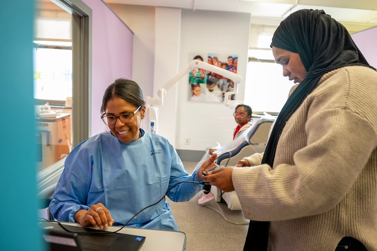 Temple dentistry student Carly Pandit works on the teeth of Andrea Jimenez, 6, as her mother, Soribel Acosta, entertains sister Sayra Jimenez, 7, who is waiting her turn in the chair at the Dental Clinic at William D. Kelley School.