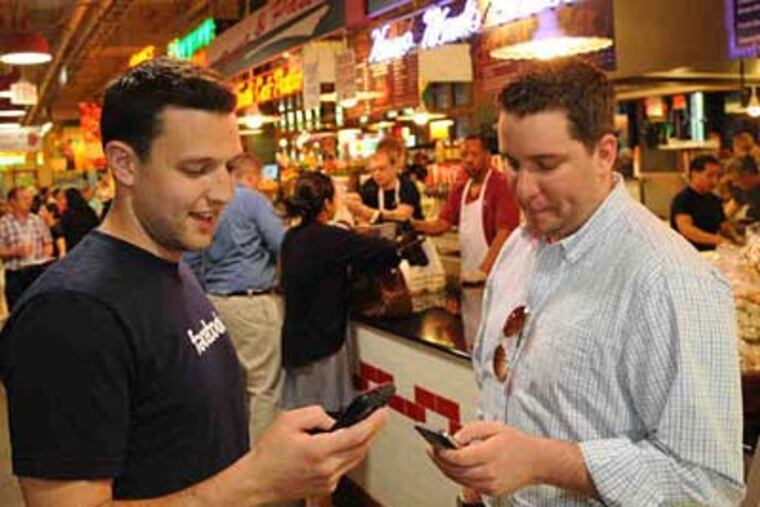 Jed Singer (left) and Jack Jokinen, a fellow Foursquare enthusiast, up- date their location on the popular application. They're in Reading Terminal Market getting lunch, and "points" for the check-in. (Clem Murray / Staff Photographer)