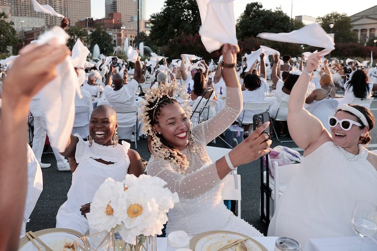 Monique Bonney of Phila (center) and Jessica Robinson of Abington (right) wave their napkins during the 10th Dîner en Blanc at Logan Square in Phila., Pa. on Aug. 18, 2022.