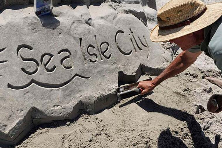 Sand sculptor Chuck Feld smooths out an identifying marker just off the boardwalk in Sea Isle City. He has been making sand creations for three decades. If done correctly, artists say, sand castles and other works can last a year or longer. TOM GRALISH / Staff Photographer