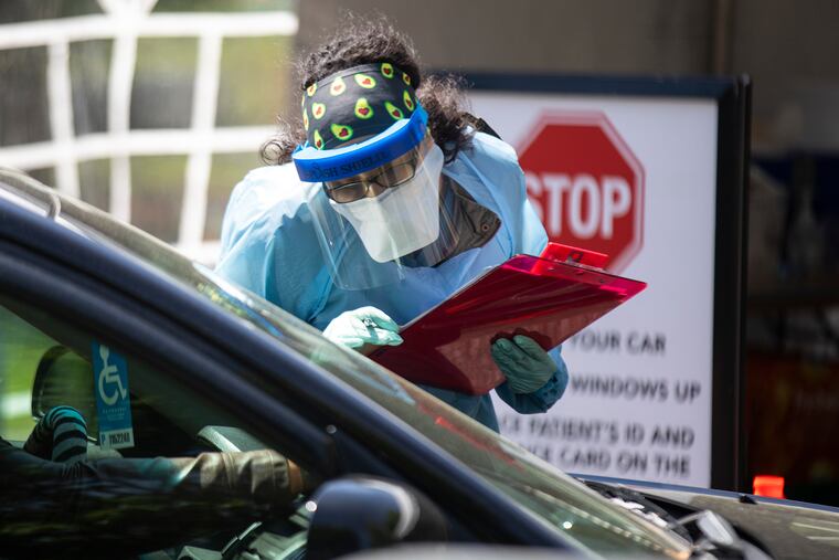 A health-care worker writes down the drivers information displayed on the dashboard of a car before testing for coronavirus in Camden on Tuesday, a coronavirus hot spot.