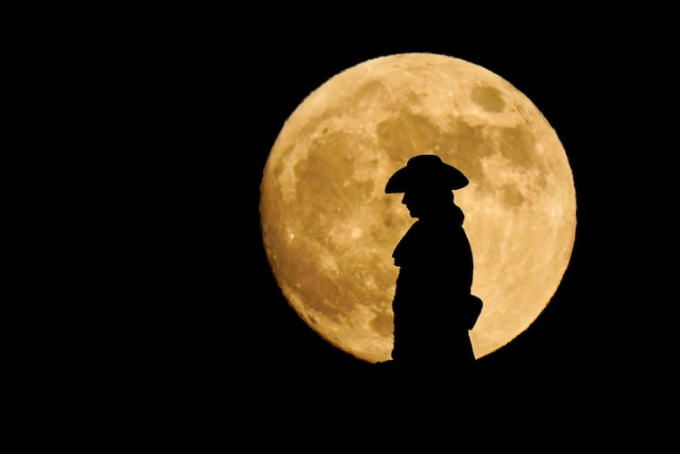 A strawberry full moon rises behind a statue of William Penn atop City Hall in Philadelphia in 2021.