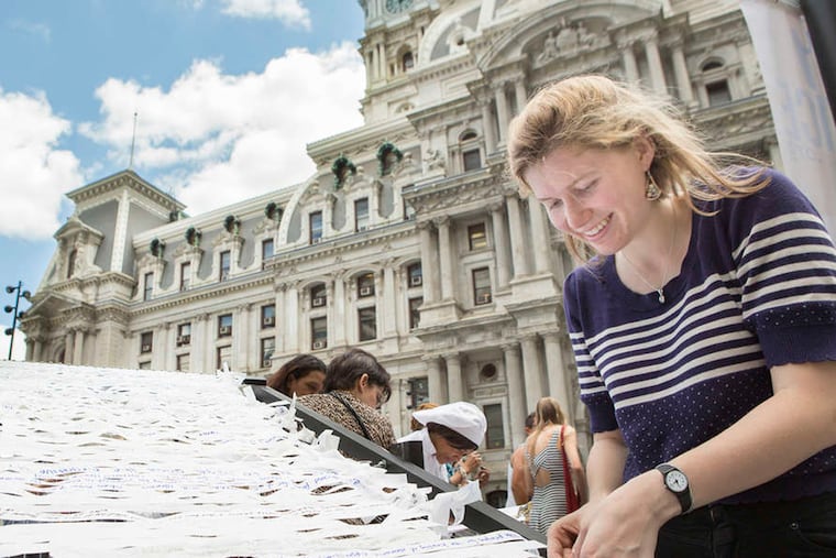 Sofia Seidel, an assistant at Meg Saligman Studios, helps participants with a public art exhibit on the grounds of City Hall. Rumination and prayer are part of the work's aim.
