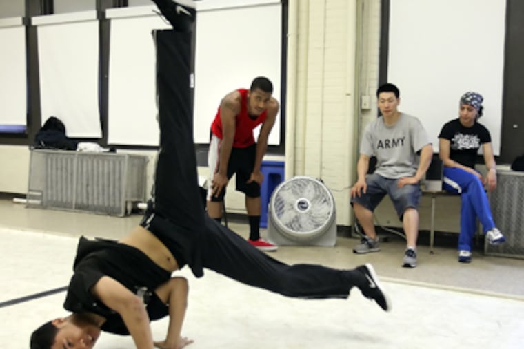 David "DK" Kruth breakdances while Benyaamin "Ben" Barnes (in red tank) and SEAMAAC dance instructors Joe Son and Candy Bloise watch in the background. (Steven M. Falk / Staff Photographer)