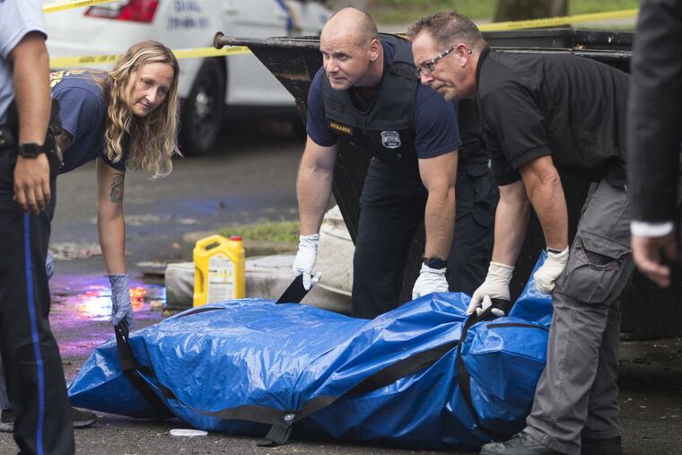 The body of a female was found inside a large suitcase in a dumpster at the Bartram Gardens Housing Project on July 17, 2018. Housing workers called the police after noticing the stench. The suitcase and body are prepred to be loaded into a police vehicle after being place in a blue bag.