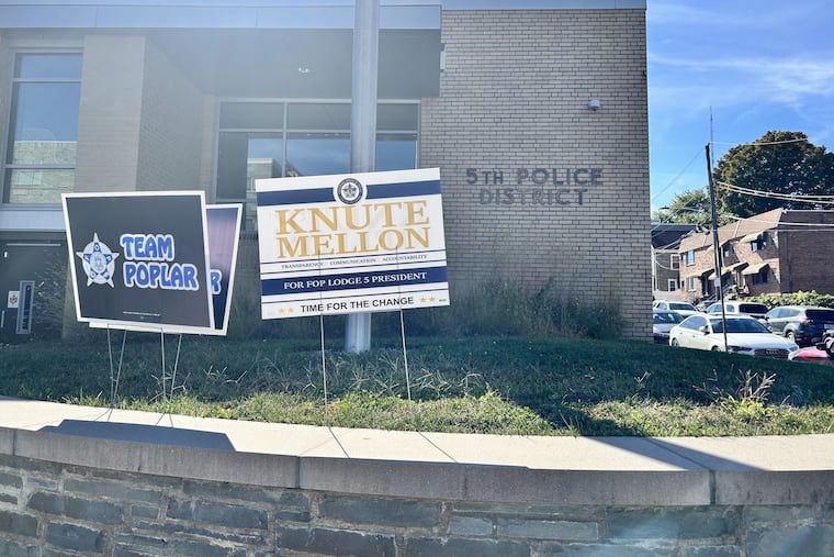 Campaign signs for Roosevelt Poplar, current president of the local police union, and his challenger, Charles "Knute" Mellon, are displayed side by side outside the 5th Police District in Roxborough. The ballots will be tallied Tuesday.