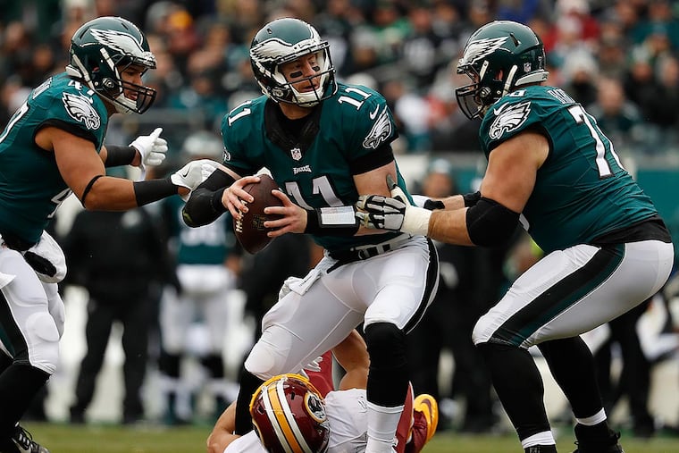 Carson Wentz (center) gets help from teammate Allen Barbre (right) as the Redskins’ Ryan Kerrigan tries to sack him.