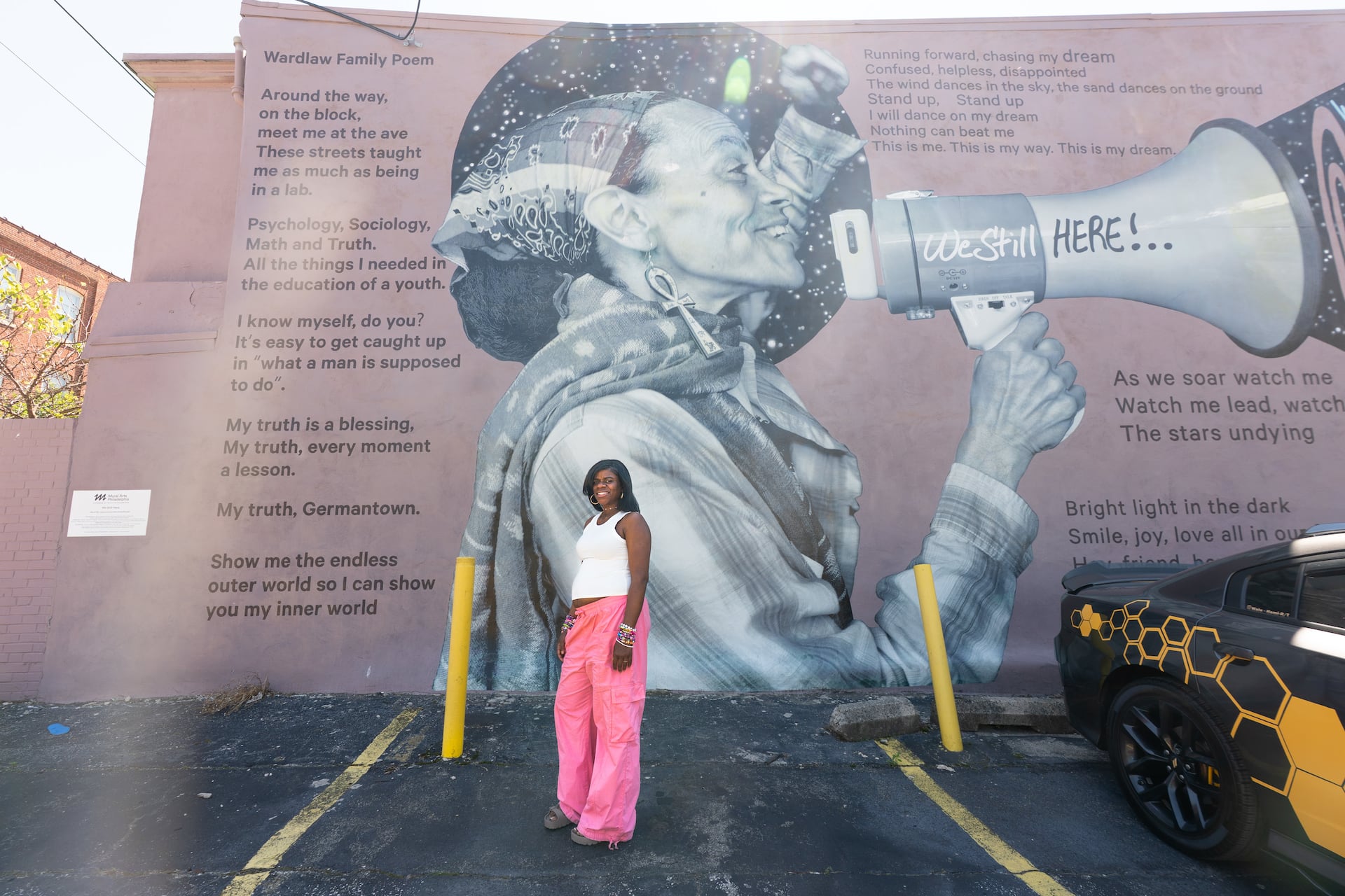 Shirley Wardlaw stands in front of the mural featuring poet and recording artist Ursula Rucker on her property, which includes a poem she wrote with her husband and daughter.