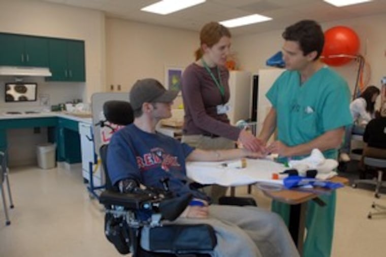 Sarah D'Emillio and physician Josh Ratner work with Josh Payette, 18, from New Hampshire. He has a spinal-cord injury, a specialty at the Shriners Hospital in Philadelphia. The facility competes with many more children's hospitals than when it was founded.