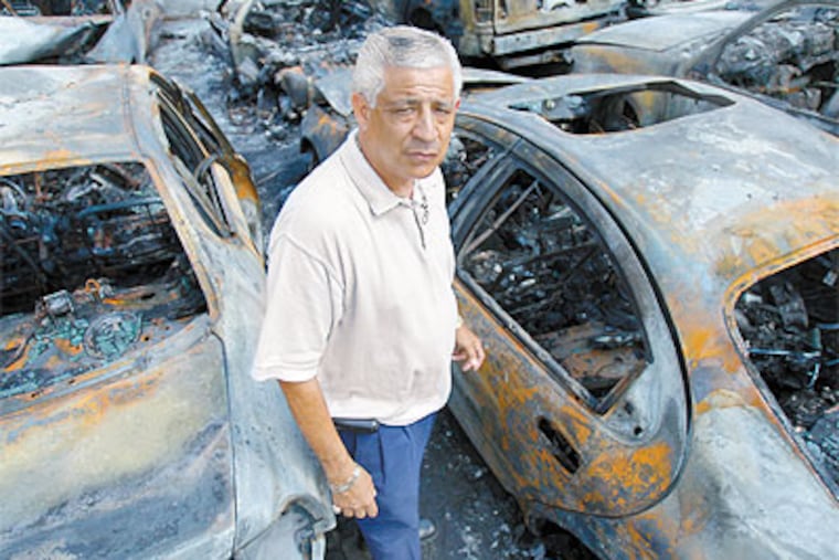 J & Sons owner Jose LaTorre Sr. stands next to cars that were set afire at his lot. (David Maialetti / Staff Photographer)