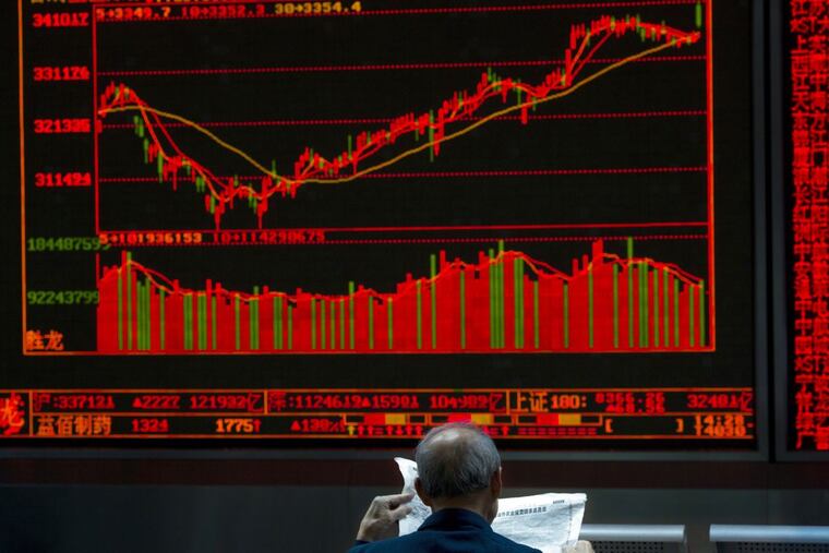An investor reads a newspaper near a graph showing the Chinese stock market index at a brokerage in Beijing on Oct. 9.