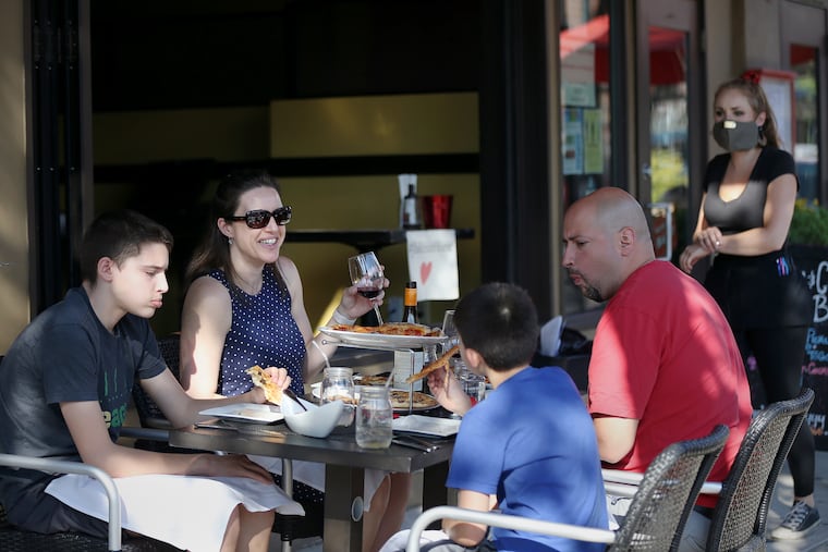 Melanie Santiago of Roxborough (second from left), her husband, Ricky (right), and their sons, Cole (left), 12, and Quinn (second from right), 9, eat pizza outside Jake's and Cooper's Wine Bar on Main Street in Philadelphia's Manayunk section on Friday, June 12, 2020. The city allowed outdoor dining to resume Friday for the first time since the city's coronavirus shutdown.