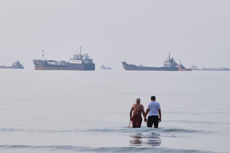 Two men wade in the waters of the Strait of Hormuz with vessels anchored in the background, off Bandar Abbas, Iran, Sunday, July 12, 2026.