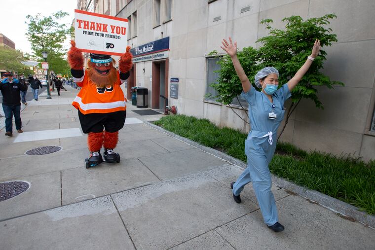 An excited Ji Su Kim, (right), a nurse anesthetist in the COVID Unit, runsdown the sidewalk as Flyers mascot, Gritty, arrives. Gritty visited the COVID Unit and led cheers for frontline responders as they made a shift change at Hospital of the University of Pennsylvania on Tuesday.