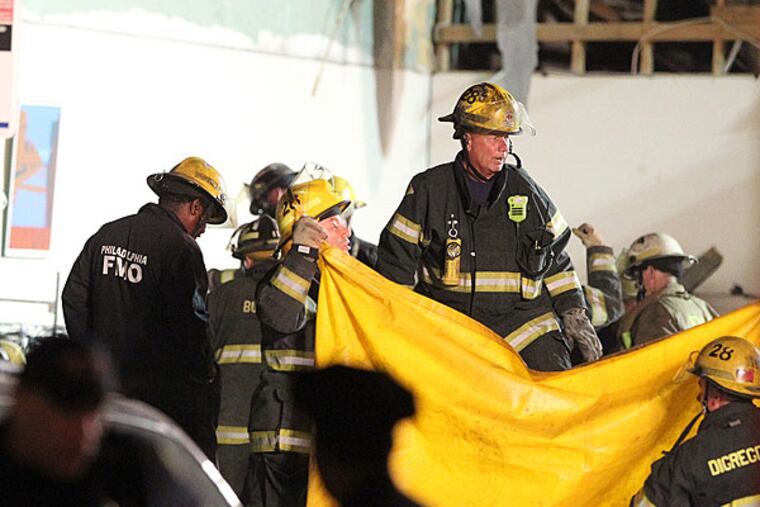 Firefighters holding up a yellow tarp as they prepared to remove another body from the rubble of the collapsed building. (CHARLES FOX / Staff Photographer)