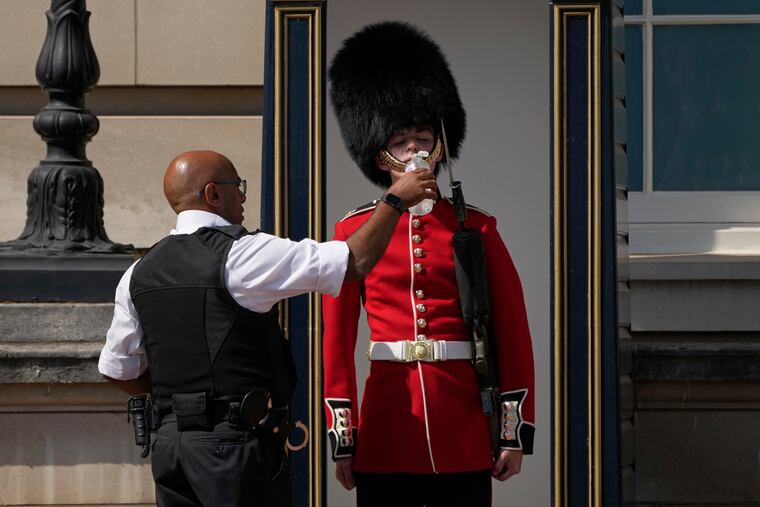 A police officer givers water to a British soldier on guard duty outside Buckingham Palace on Monday.