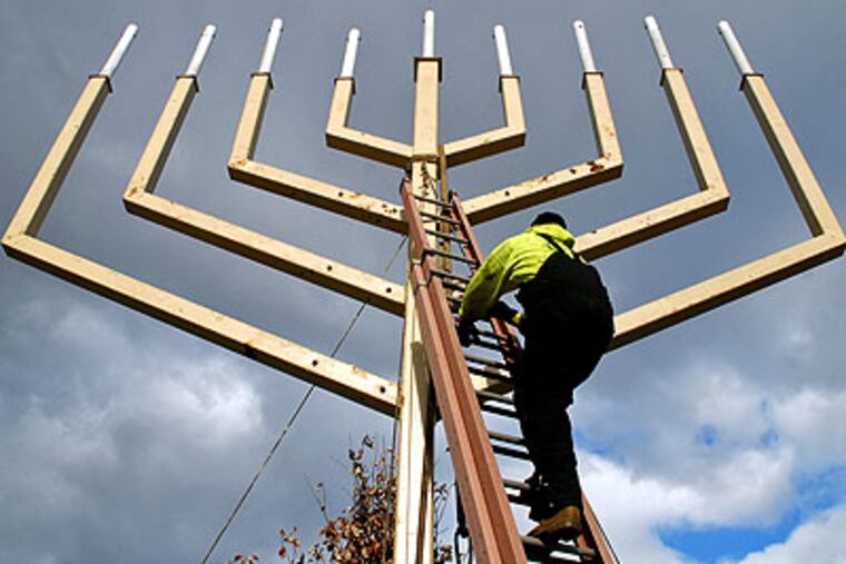 Brian Yohnnson of Moorestown unties the crane after he and co-workers from Mayberry Riggers installed the 37-foot-high menorah Thursday on Independence Mall, where it will be lit Friday evening to mark the first night of Hanukkah. (Tom Gralish / Staff Photographer)