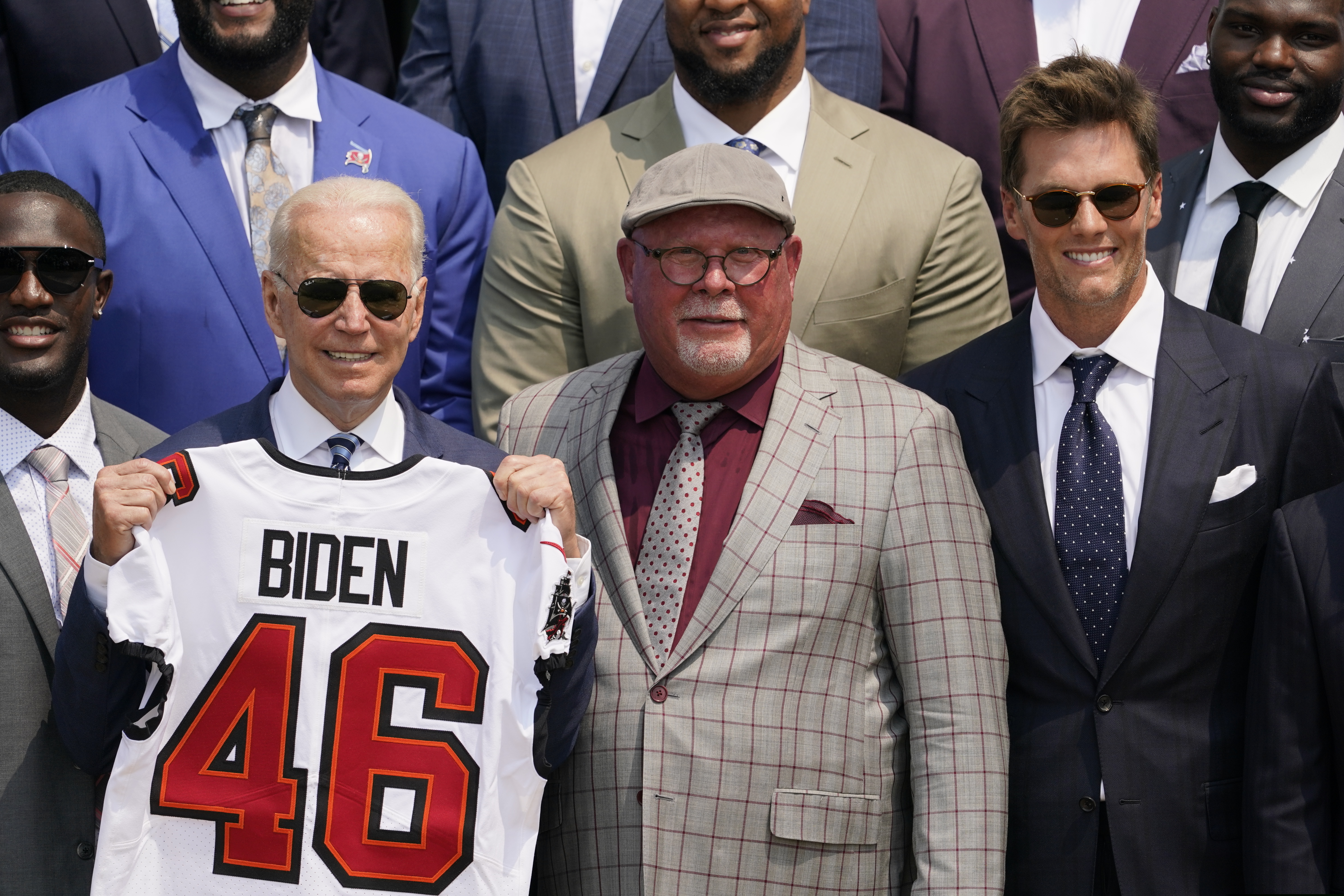 President Joe Biden, surrounded by members of the Tampa Bay Buccaneers, poses for a photo holding a jersey during a ceremony on the South Lawn of the White House.