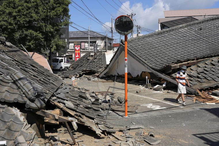 A person walks past the houses collapsed in an earthquake in Yatsushiro, Kumamoto Prefecture, southern Japan, Friday, July 31, 2026.