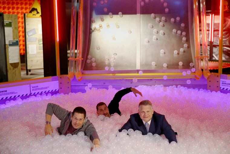 From left, authors Josh Piven and David Borgenicht and Franklin Institute President and CEO Larry Dubinski try out the avalanche scenario in the ball pit of the "Worst Case Scenario" exhibit at the Franklin Institute.
