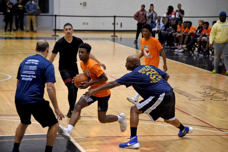 Parkway Center City Middle College sophomore Zubayr Ray drives to the basket while facing defenders (from left) Officers Joe Gutierrez, Omar Torres, and Cliff Mobley from the Ninth Police District.