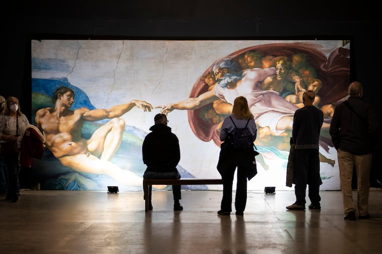 Visitors take in "The Creation of Adam" at Michelangelo's Sistine Chapel exhibition at the Fashion District in Philadelphia, Pa. on Wednesday, January 26, 2022. The 2-story exhibit features recreations of Michelangelo's Sistine Chapel ceiling frescos and the Last Judgement.